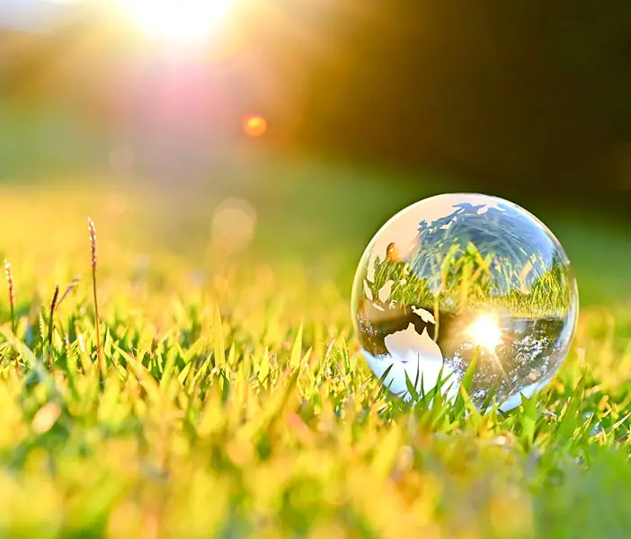草の上に置かれた世界地図が描かれた透明なガラス球体と太陽光
