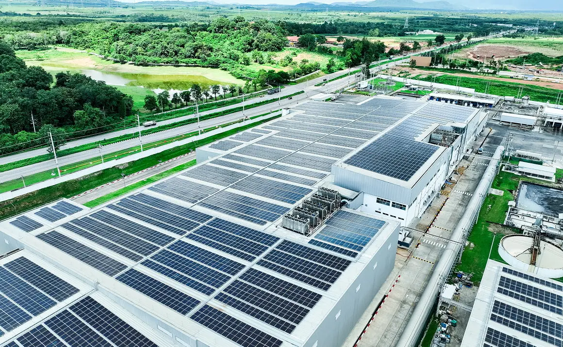 緑の風景に囲まれた、屋根全面に太陽光パネルを備えた産業施設の空撮