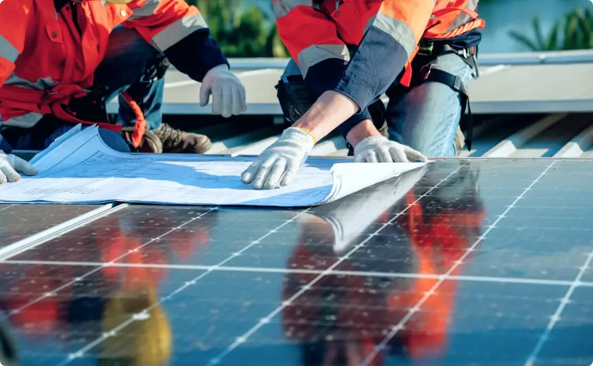 太陽光パネル上で図面を確認しながら打ち合わせをする作業員