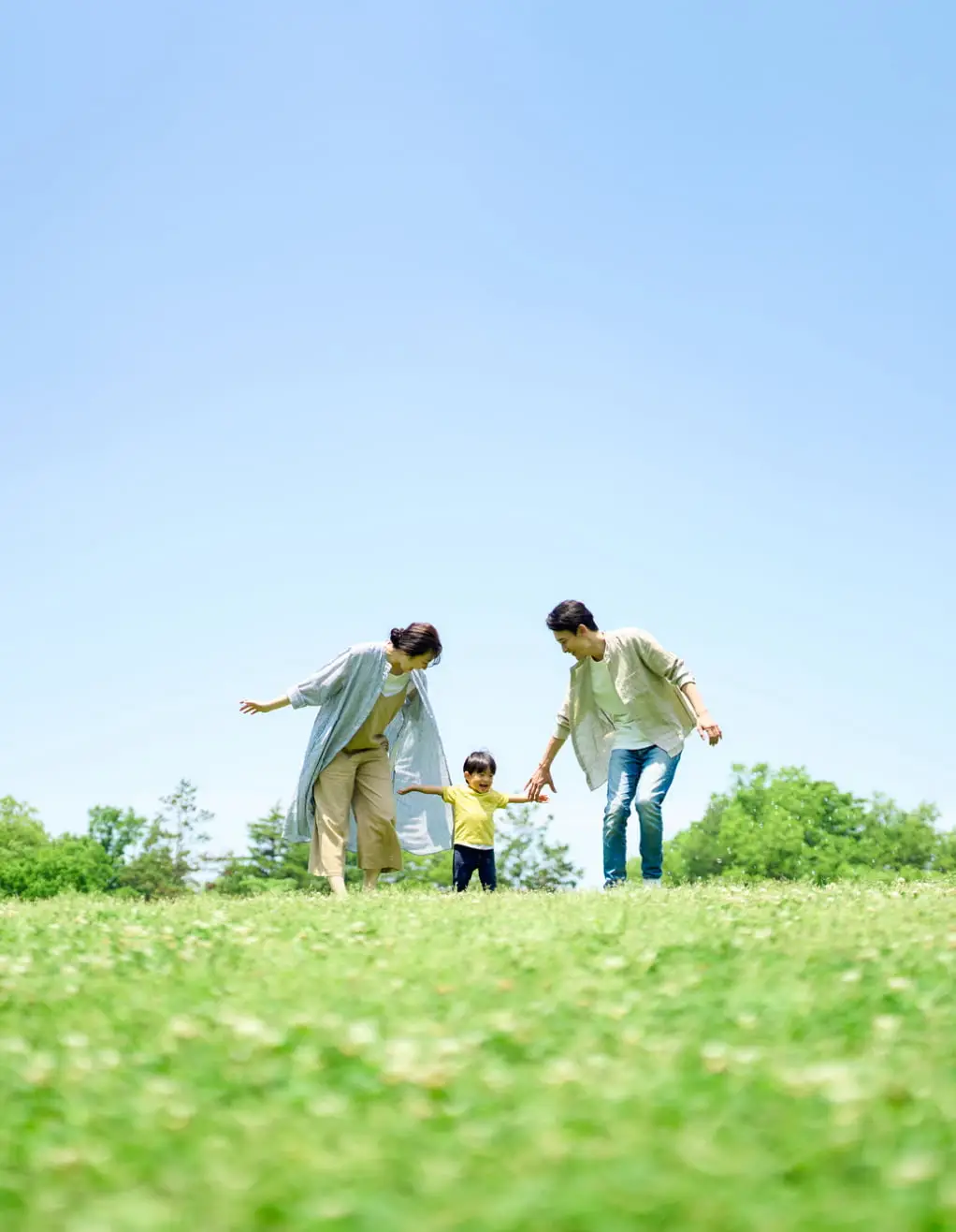 青空の下、広い草原で家族が楽しそうに過ごす様子。未来を担う子供と家族の幸せな時間を表現しています。