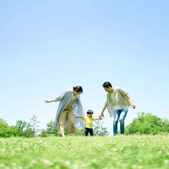 青空の下、広い草原で家族が楽しそうに過ごす様子。未来を担う子供と家族の幸せな時間を表現しています。