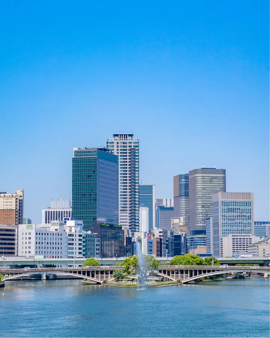晴れた日の近代的な都市の景観。青い川に架かる白い橋と、川の向こう岸に立ち並ぶ高層ビル群