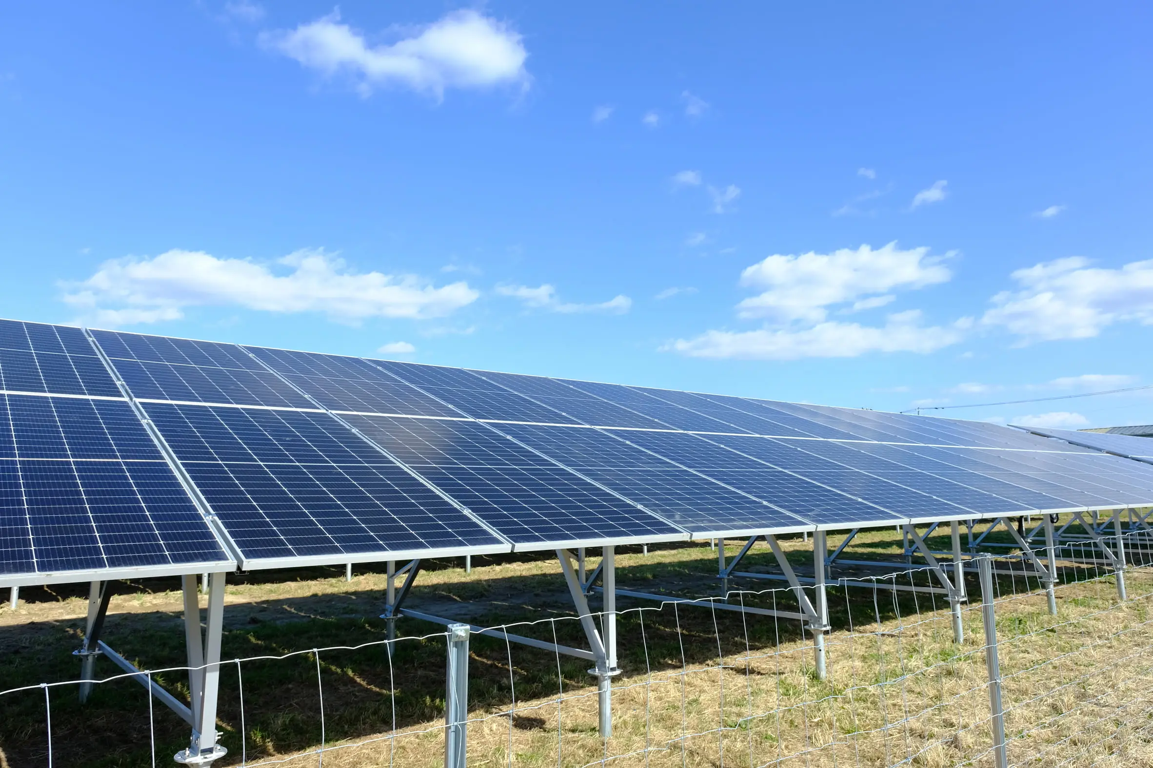 青空と白い雲が広がる下、多数の太陽光パネルが設置された風景