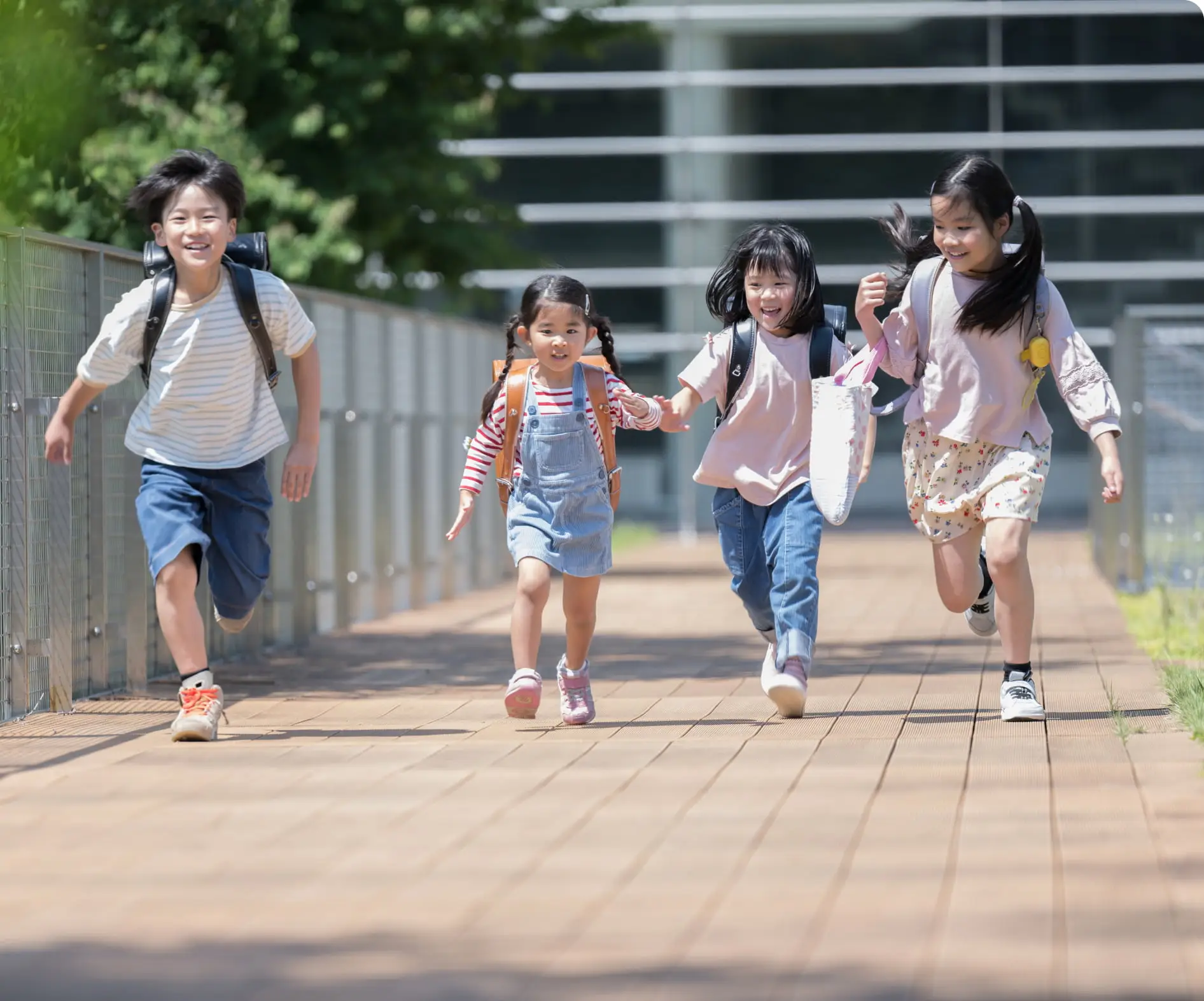 明るい日差しの下、舗装された道を元気いっぱいに走る笑顔の子供たちの風景