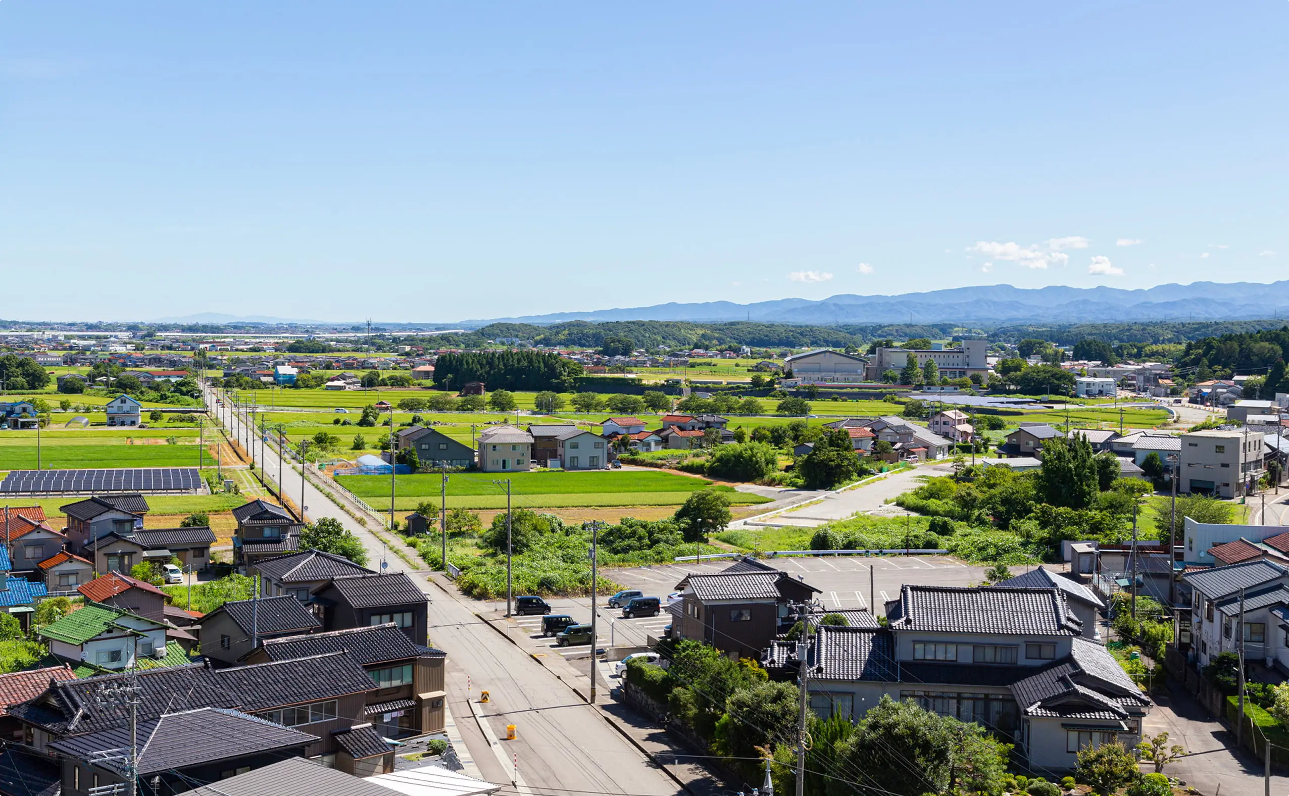 青空の下、伝統的な家々と緑豊かな田園風景の中に太陽光パネルが設置された日本の農村の眺望
